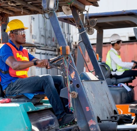 African American foreman or cargo container worker drive cargo car beside of his co-worker woman in workplace area. Industrial support system help employee performance concept.